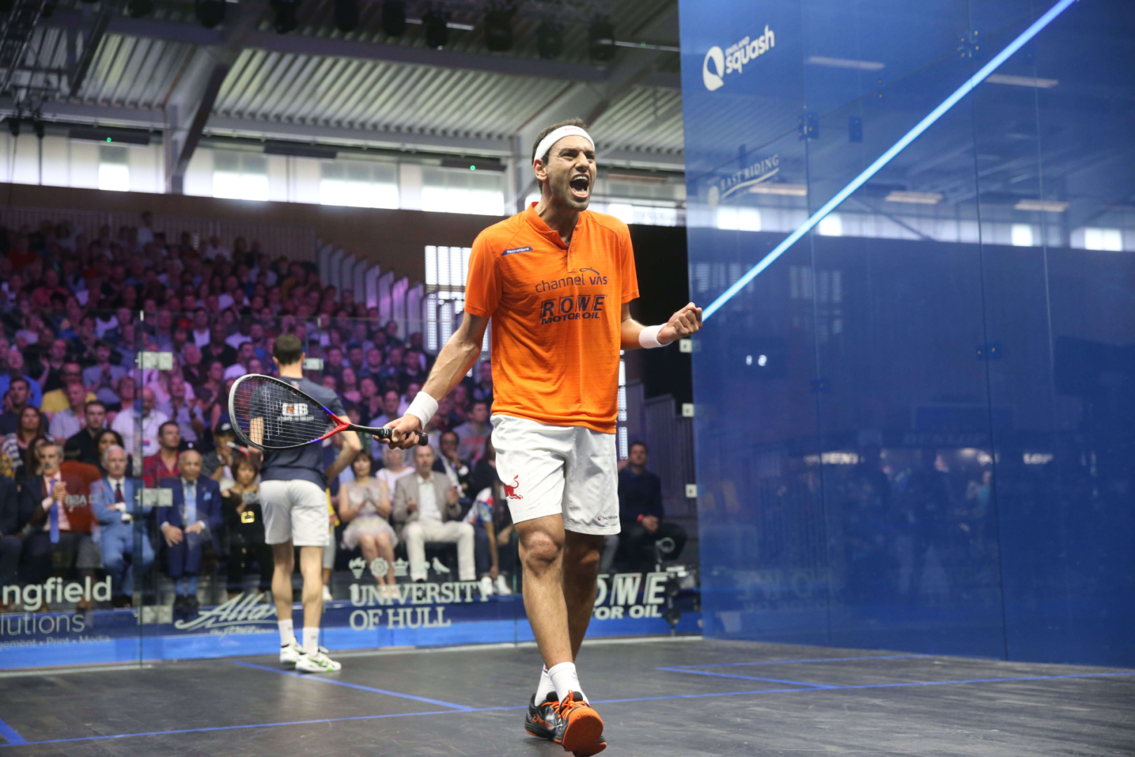 2 men playing squash in a court in front of a crowd
